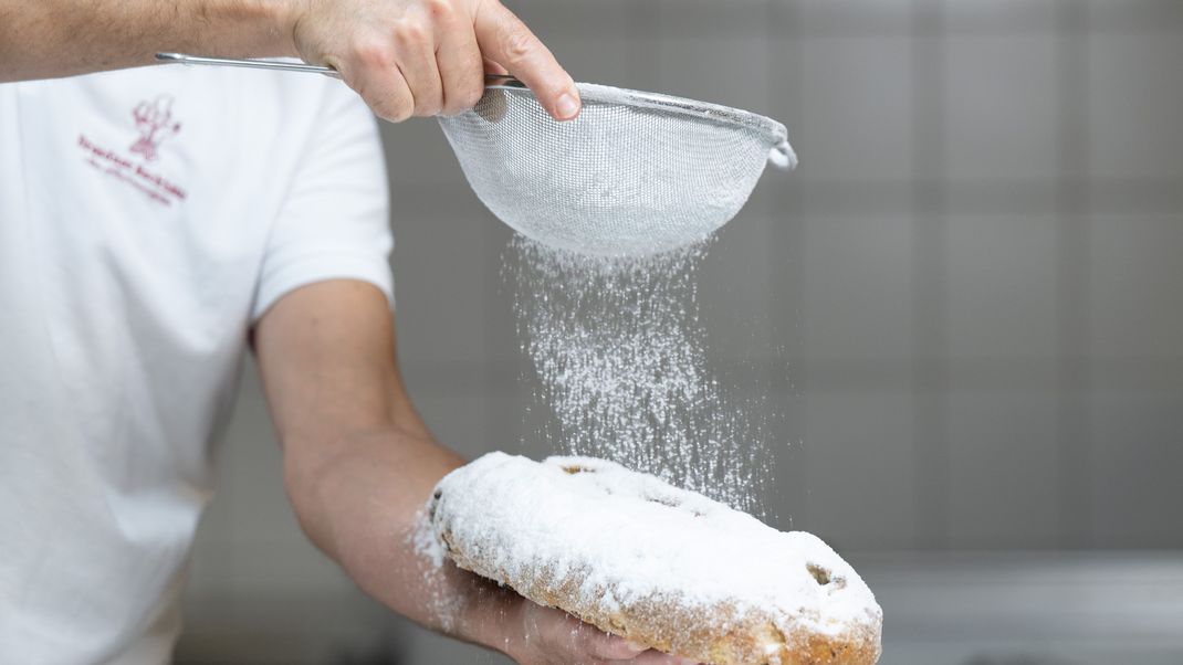 Ein Bäcker bestreut im Dresdner Backhaus einen Christstollen mit Puderzucker.