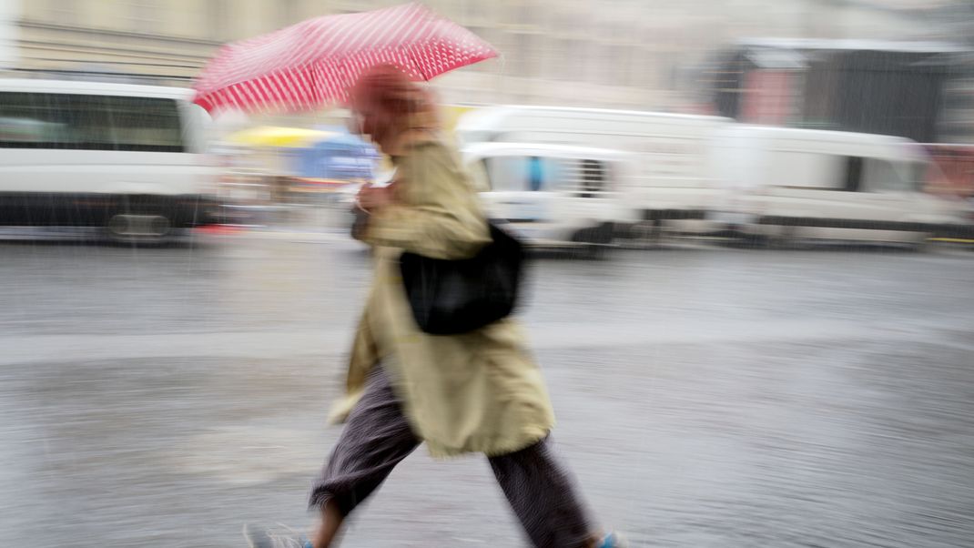 Eine Frau mit rotem Regenschirm geht bei starkem Regen über den Odeonsplatz in der bayerischen Landeshauptstadt.