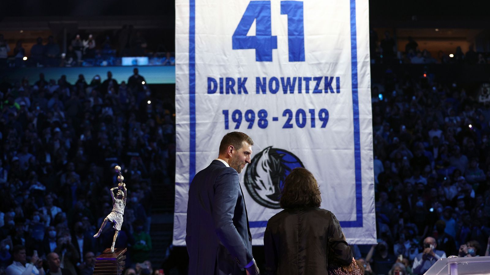 
                <strong>Der Moment - das Trikot geht unter das Hallendach</strong><br>
                Dann ist es soweit. Die Mavericks ziehen Nowitzkis 41 unter das Hallendach. Mit Ehefrau Jessica und den Kindern verfolgt der Würzburger die Zeremonie.
              