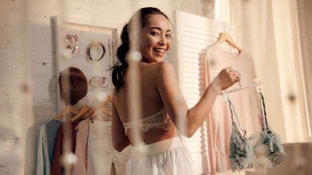 beautiful asian girl holding hanger with lace bralette and smiling at camera