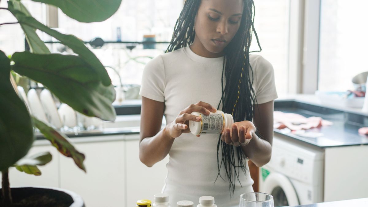 African American woman taking vitamins and supplements at home in her kitchen