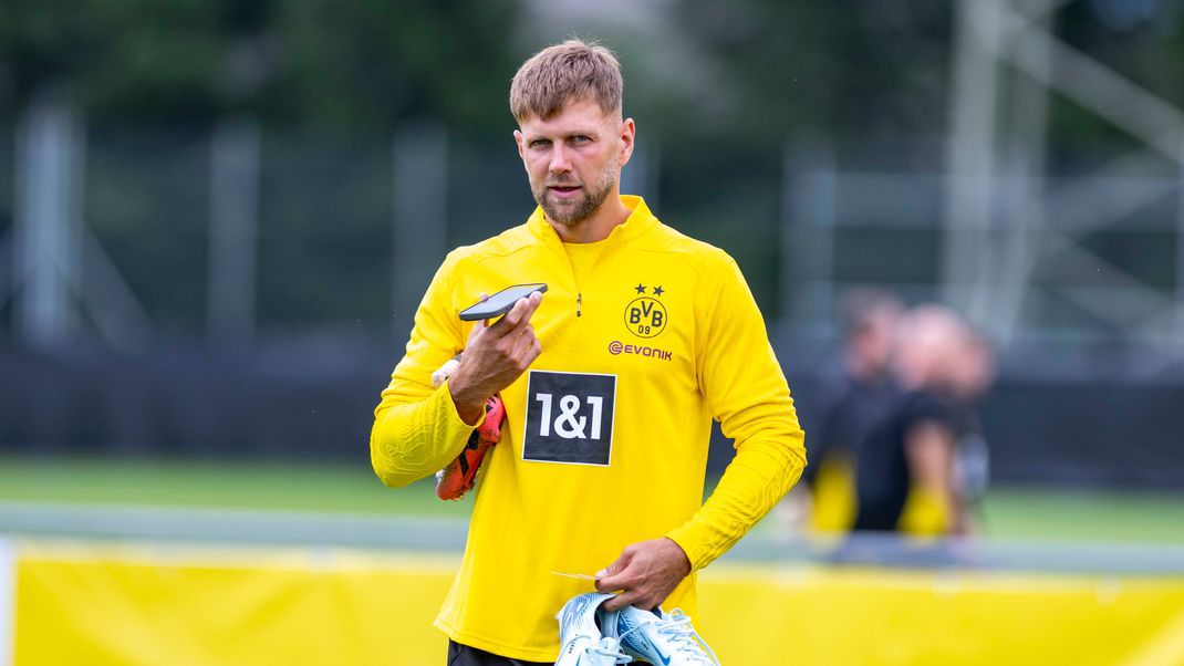 Niclas Füllkrug hält seine Fußballschuhe in der Hand und spricht in sein Smartphone.