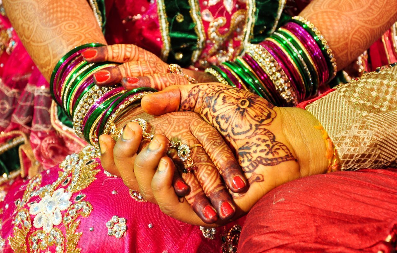 Hochzeit in Henna: In Indien ist es Brauch, in der Nacht vor dem großen Tag Hände und Füße der Braut kunstvoll mit dem roten Farbstoff aus den Blättern des Hennastrauchs zu bemalen. Früher übernahm das meist ein Familien- oder Verwandtschafts-Mitglied, heute wird dafür gern ein:e Henna-Künstler:in engagiert. Mancherorts bekommt auch der Bräutigam ein Mendhi (oder Mehendi). Die ornamentale Körperbemalung symbolisiert den heili
