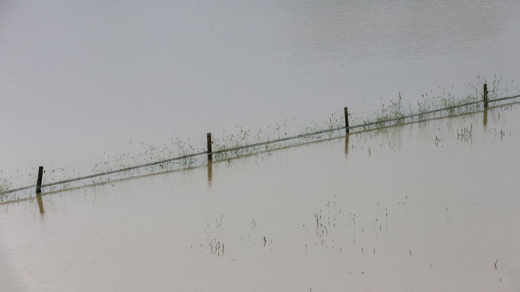  Ein Weidezaun und einzelne Grashalme ragen aus einer vom Regen überfluteten Wiese in Riedlingen, Baden-Württemberg.