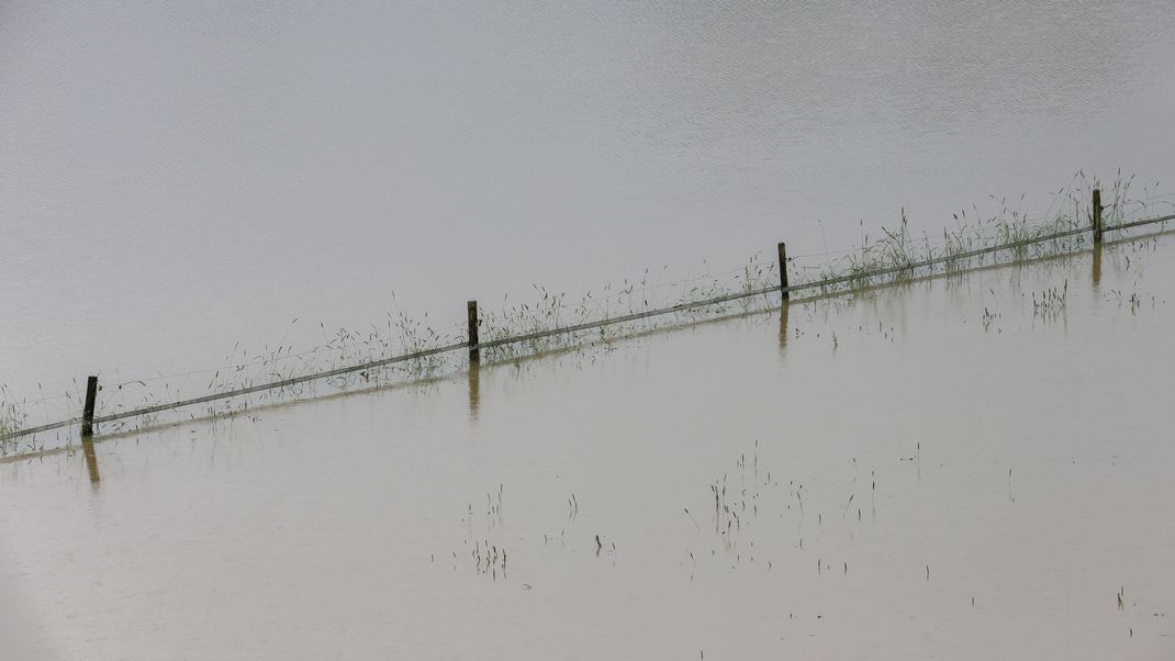  Ein Weidezaun und einzelne Grashalme ragen aus einer vom Regen überfluteten Wiese in Riedlingen, Baden-Württemberg.