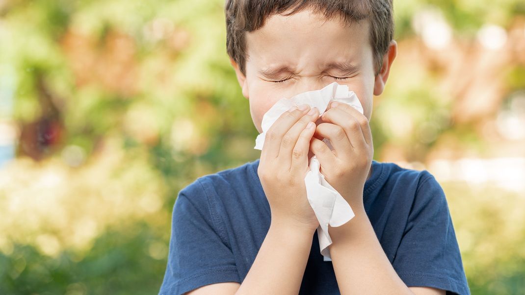 Allergic child sneezing covering nose with wipe in a park in spring or summer season