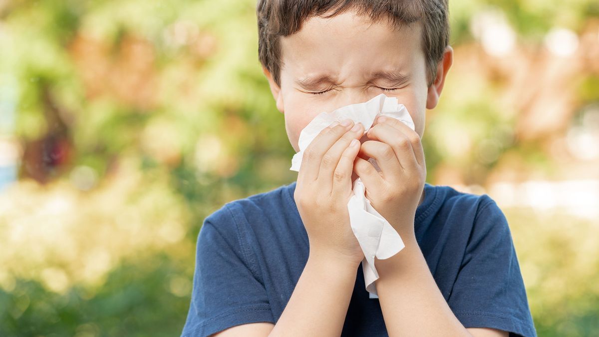 Allergic child sneezing covering nose with wipe in a park in spring or summer season