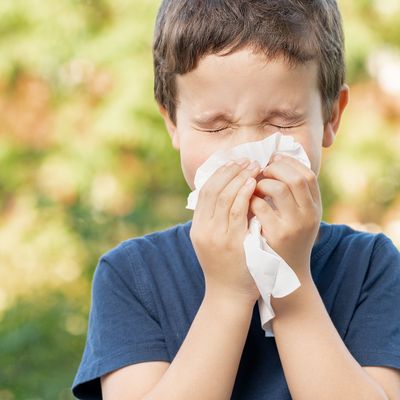 Allergic child sneezing covering nose with wipe in a park in spring or summer season