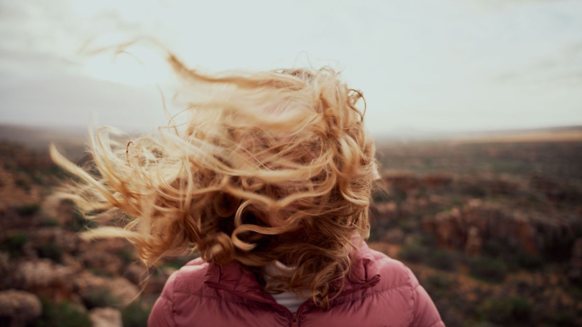Closeup of young woman face covered with flying hair in windy day standing at mountain
