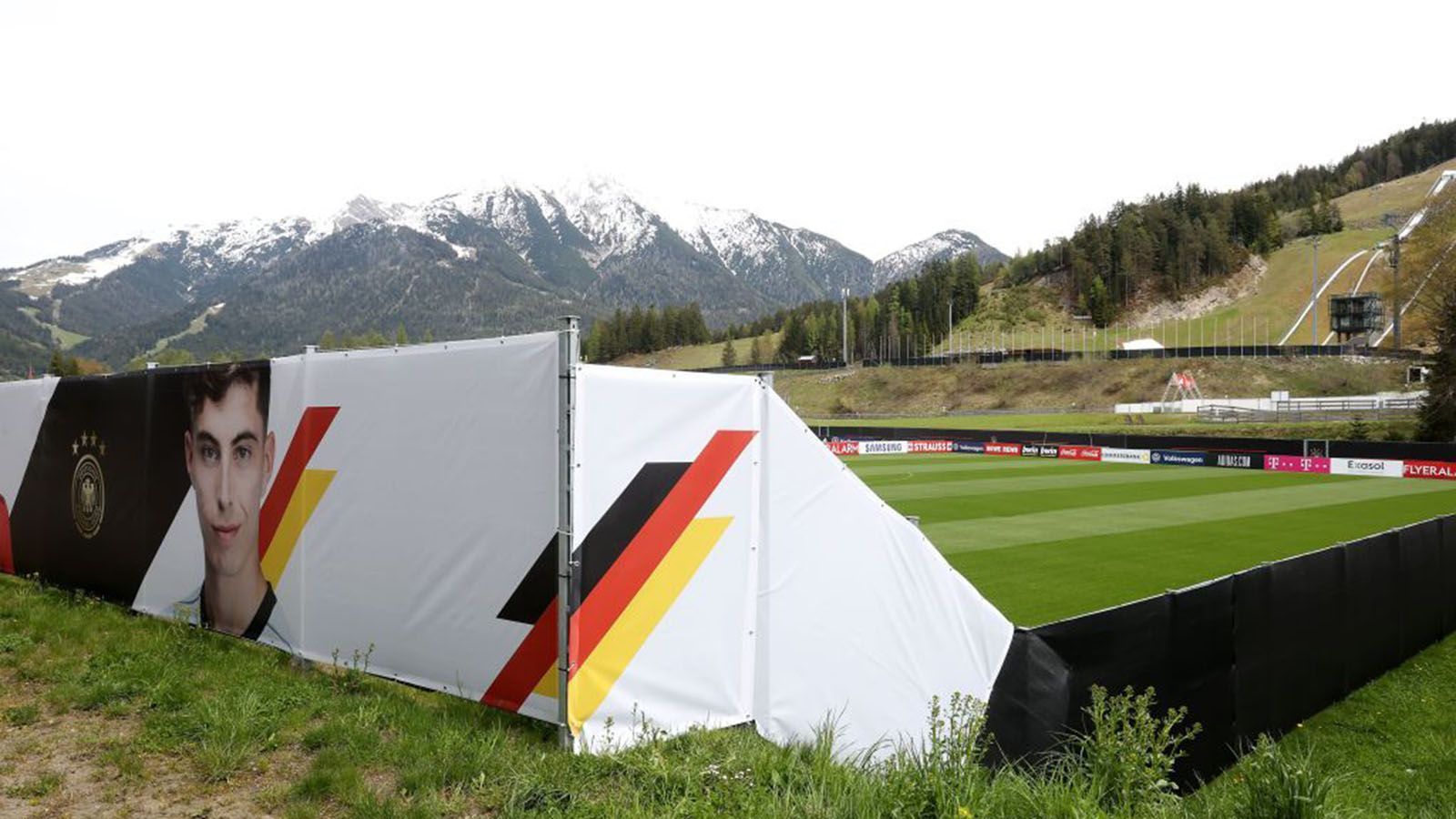 
                <strong>Das luxuriöse DFB-Quartier im Trainingslager in Seefeld</strong><br>
                Beim Trainingsplatz der Nationalmannschaft am Hotel in Seefeld errichtete der Deutsche Fußball Bund einen Zaun rund um den grünen Rasen. Dafür gab die Gemeinde dem DFB eine Ausnahmegenehmigung. Grund dafür ist nicht primär der Sichtschutz, der, wie man im Bild sieht, seinen Zweck verfehlen würde, sondern Hygienemaßnahmen. Die Ansammlung von Zuschauern und Kiebitzen vor dem Gelände soll dadurch verhindert werden.
              