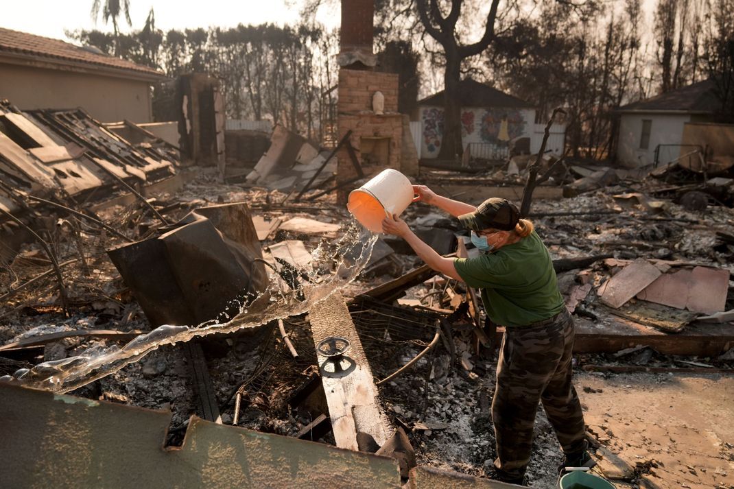 Anwohnerin Nancy Belanger gießt Wasser auf das vom Feuer verwüstete Grundstück eines Nachbarn nach dem Palisades-Brand im Stadtteil Pacific Palisades von Los Angeles.