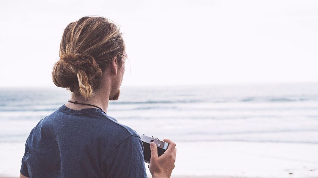 Der klassische Man Bun wird tief im Nacken getragen – dabei spielt es keine Rolle, ob dieser mit glatten Haaren oder mit Locken gestylt wird.