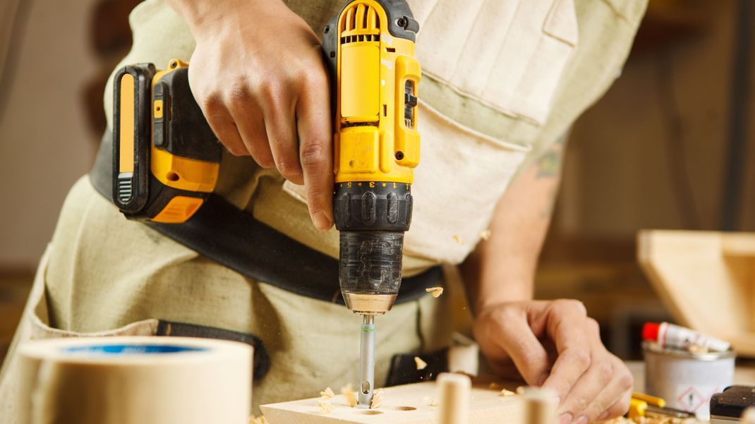 Heimwerker bohrt mit seiner Bohrmaschine mehrere Löcher in Holz.