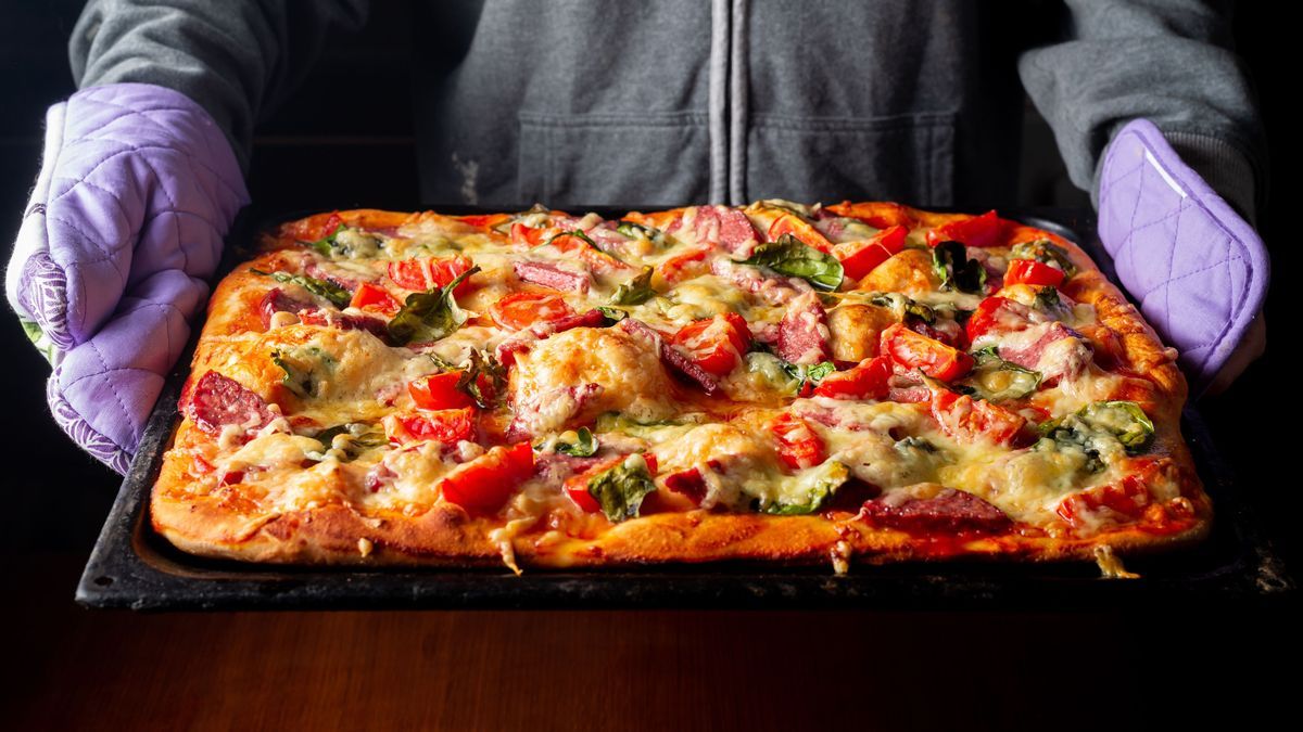 Ready pizza in hands on a baking sheet in hands in the kitchen at home.