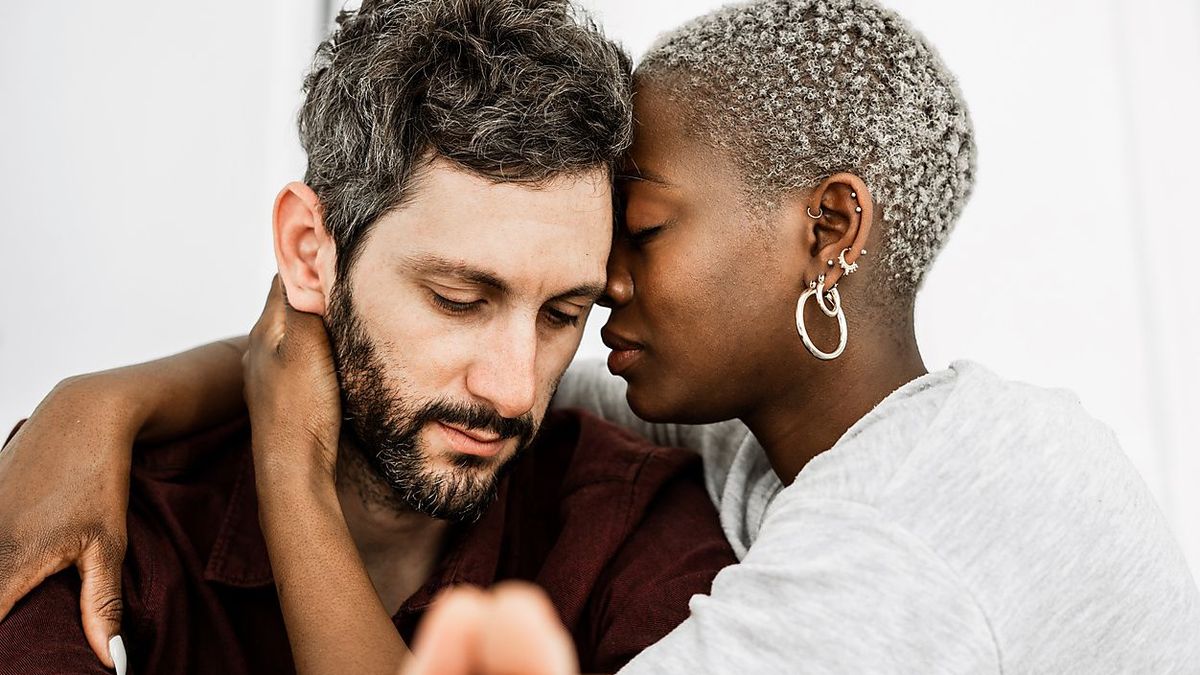 Side view of gentle multiethnic couple hugging while resting at table in modern kitchen with closed eyes