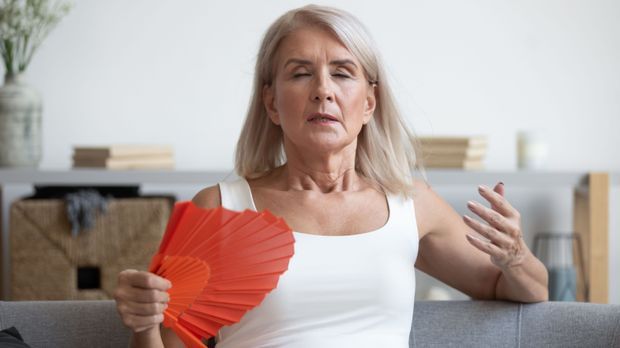 Ältere Frau mit Fächer kämpft gegen Hitzewallungen in den Wechseljahren.