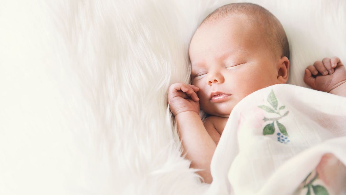 Sleeping newborn baby in a wrap on white blanket.