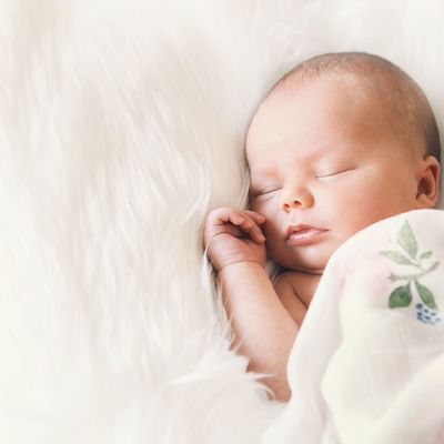 Sleeping newborn baby in a wrap on white blanket.
