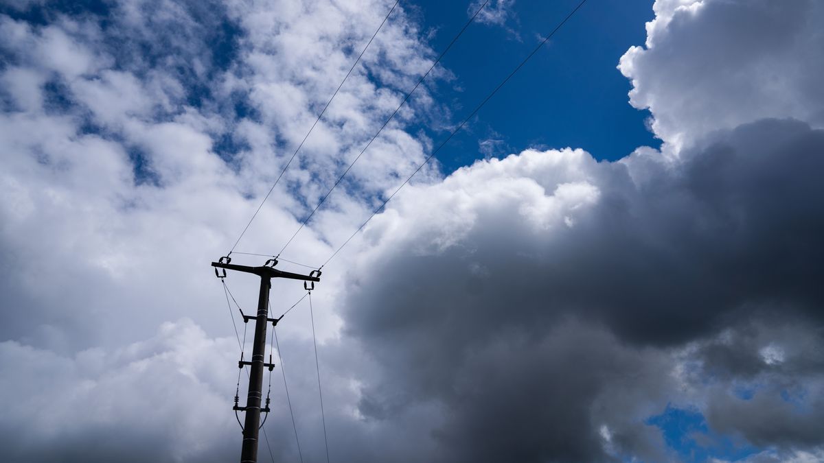 Ein Strommast hebt sich vor dem stark bewölkten Himmel ab. 
