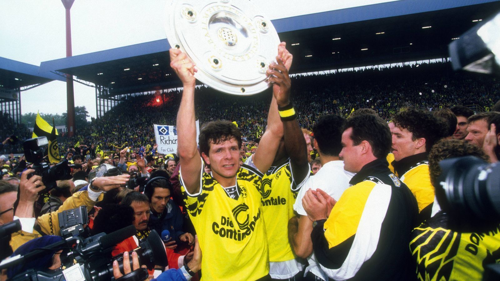 
                <strong>Borussia Dortmund (Saison 1994/95)</strong><br>
                Der FC Bayern spielte eine schwache Saison 1994/95, die nur auf Platz 6 endete. Doch im Endspurt wurde der Rekordmeister zum Zünglein an der Waage im Titelkampf zwischen Dortmund und Bremen. Mit einem 3:1-Sieg am 34. Spieltag gegen den damaligen Tabellenführer Werder Bremen lieferte der FCB eine Steilvorlage für den BVB. Die Dortmunder ließen sich im Heimspiel gegen den HSV nicht zweimal bitten, gewannen dank Treffern von Andreas Möller (v.) und Lars Ricken mit 2:0. So überholte die Borussia Werder noch und beendete die Saison mit einem Punkt Vorsprung als Meister. Pikant: Der damalige Werder-Trainer Otto Rehhagel wechselte nach der Saison 1994/95 zum FC Bayern, also jenem Verein, der "König Ottos" meisterlichen Abschied aus Bremen verhinderte.
              