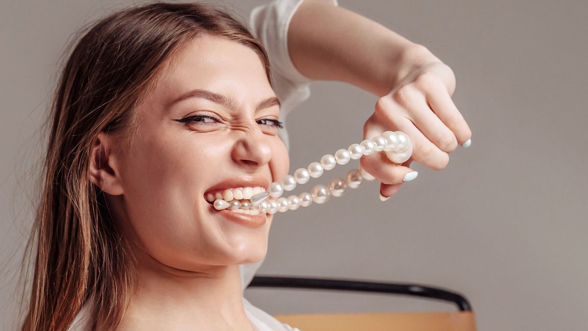 Girl holding pearl beads in her teet. Beautiful smile and white teeth of a young woman. 