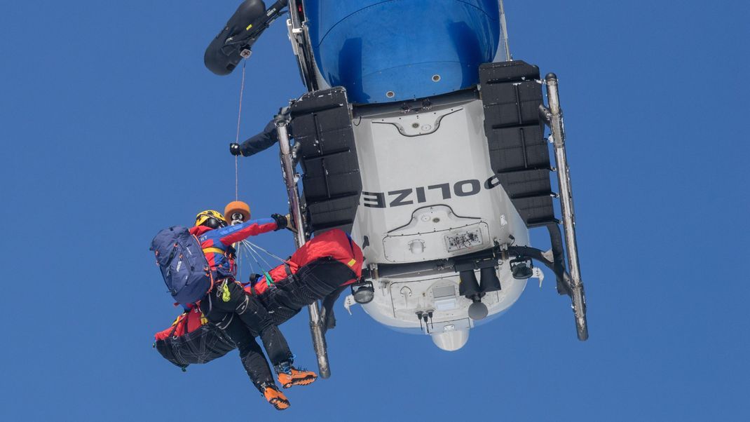 Archivbild: Ein Bergwachtmann und ein geretteter Mensch werden in Bayern bei einer Lawinenübung des Alpinen Einsatzzuges der Polizei und Bergwacht in einen Polizeihubschrauber gezogen.