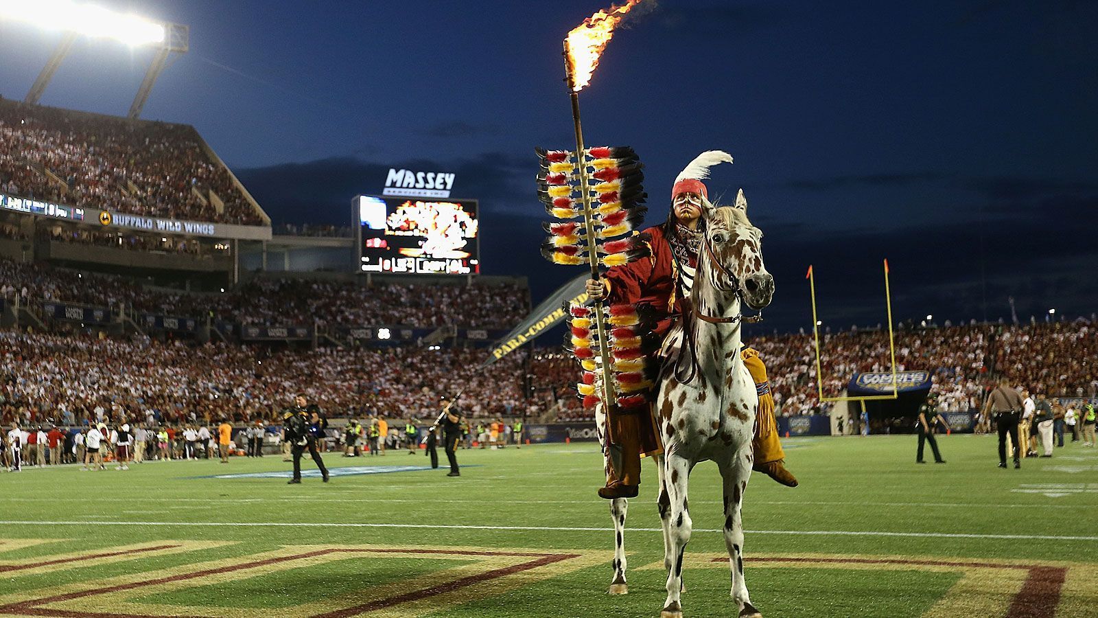 
                <strong>Osceola und Renegade (Florida State Seminoles)</strong><br>
                Die Teams der Florida State University können sich auf Chief Osceola - der ein Mitglied des Indianerstammes der Seminolen darstellt - und sein Appaloosa Renegade verlassen. Ersterer ist mit einem brennenden Speer ausgestattet, den er vor dem Kickoff in der Mitte des Feldes in den Rasen pflanzt. Vor dem ersten Erscheinen des Duos 1978 waren bereits verschiedene Maskottchen aktiv - stets ging es dabei um die Darstellung von Ureinwohnern Amerikas. Bereits 1962 kam die Idee auf, ein reitendes Maskottchen einzuführen, doch erst mit der Unterstützung der Frau des damaligen Football-Head-Coaches ließ sich der Plan letztlich umsetzen. Trotz diverser Kontroversen um das Indianerkostüm an sich und den Kopfschmuck im Besonderen hält sich die Tradition mittlerweile seit mehr als vier Jahrzehnten.
              