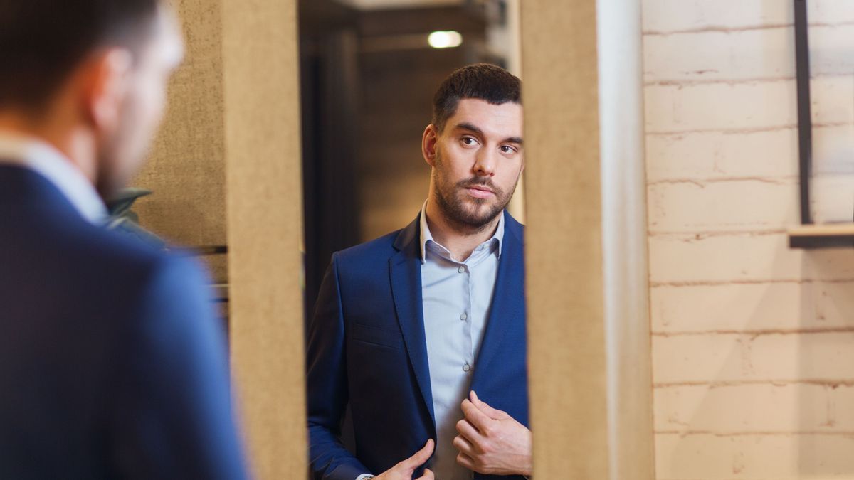 man trying jacket on at mirror in clothing store