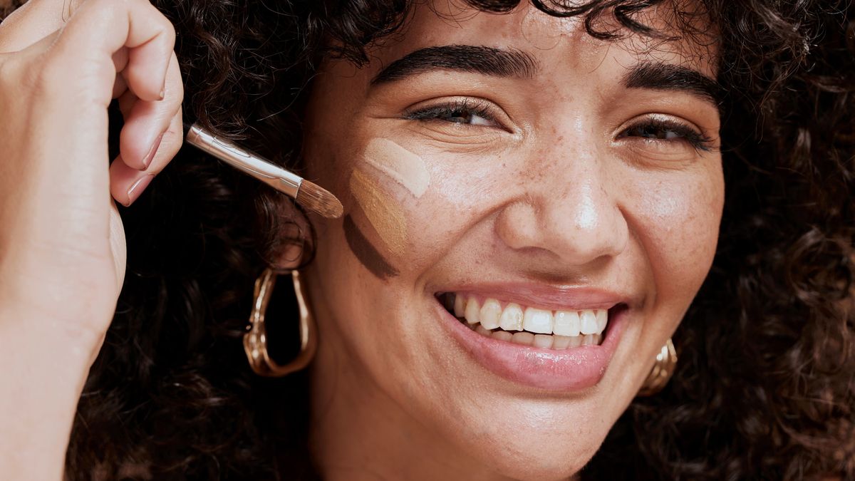 Face, makeup and brush with a woman black model applying foundation to her skin in studio for cosmetics. Portrait, wellness and luxury with an attractive young female using a cosmetic product