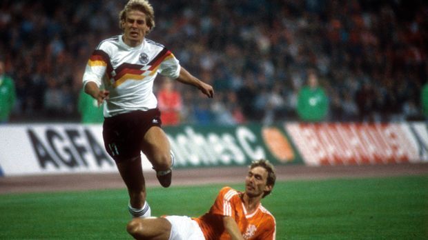 
                <strong>EM 1988 (Jürgen Klinsmann)</strong><br>
                EM 1988: Bei der Europameisterschaft im eigenen Land bringen Jürgen Klinsmann und Co. zum ersten Mal Farbe ins Spiel. Mit einem schwarz-rot-goldenem Band auf der Brust wird die Trikotgestaltung mutiger. Es bringt dennoch nichts: Deutschland verliert im Halbfinale gegen die Niederlande. 
              