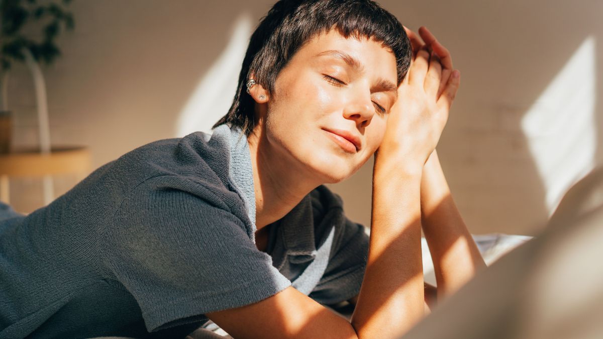 A woman lies on a bed in bright sunlight from the window.