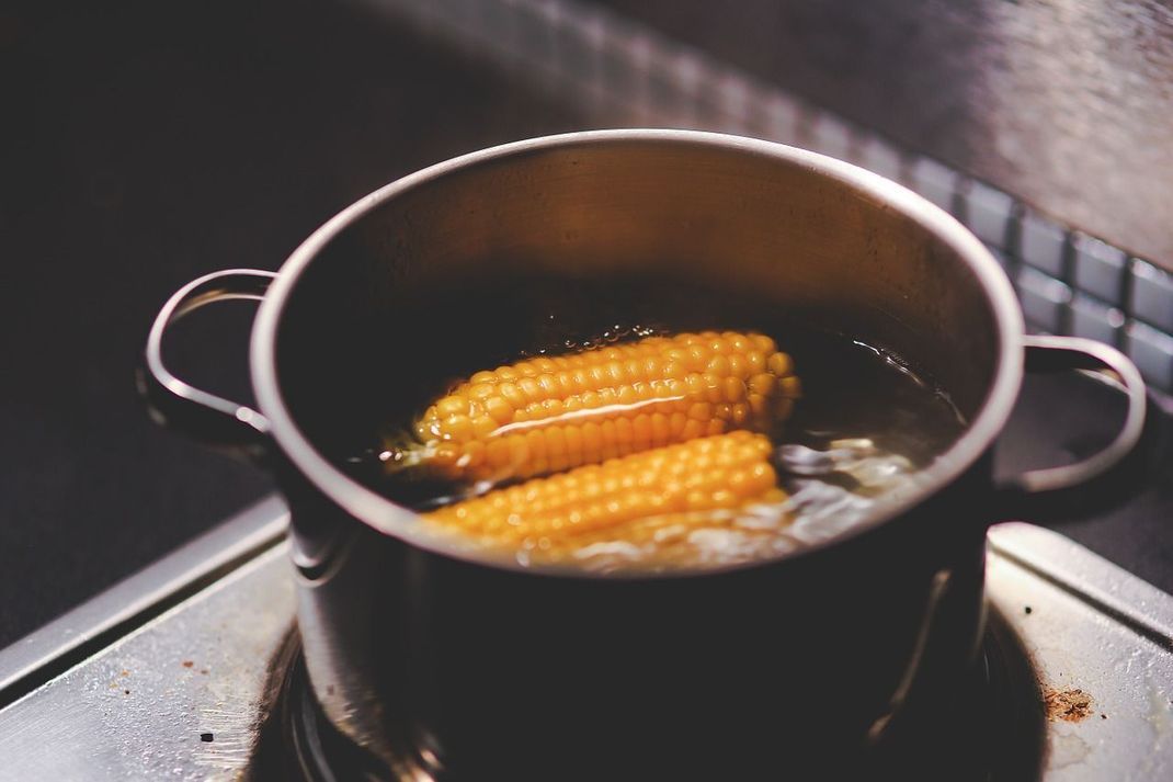 Bevor Sie die Maiskolben grillen, sollten Sie diese in kochendem Wasser vorgaren.