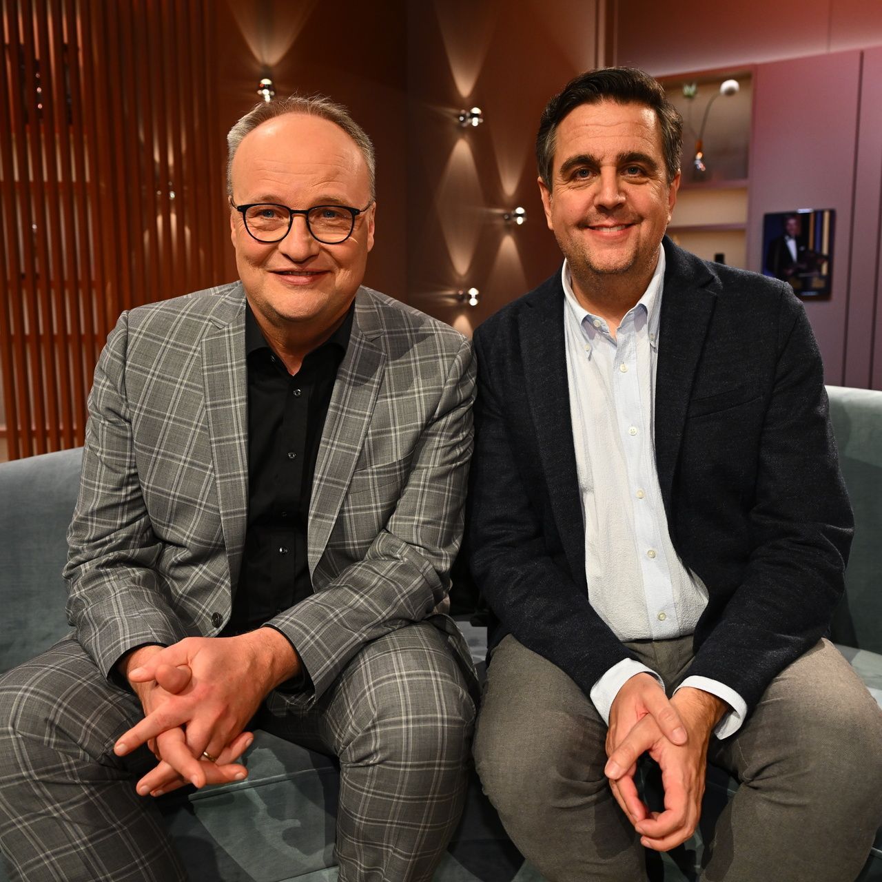 Oliver Welke (l.) und Bastian Pastewka (r.) sitzen auf dem Fernsehsofa im Set ihrer Überraschungsshow "Welke & Pastewka - Wiedersehen macht Freude!".