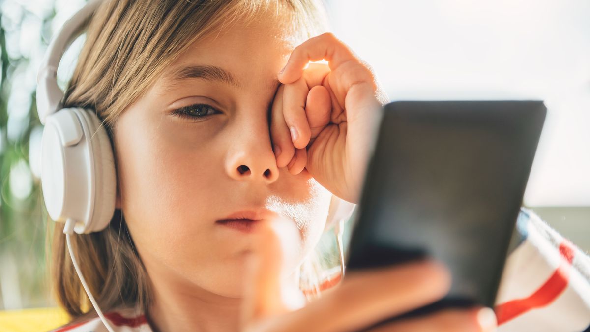 Tired Little girl with headphones using smart phone