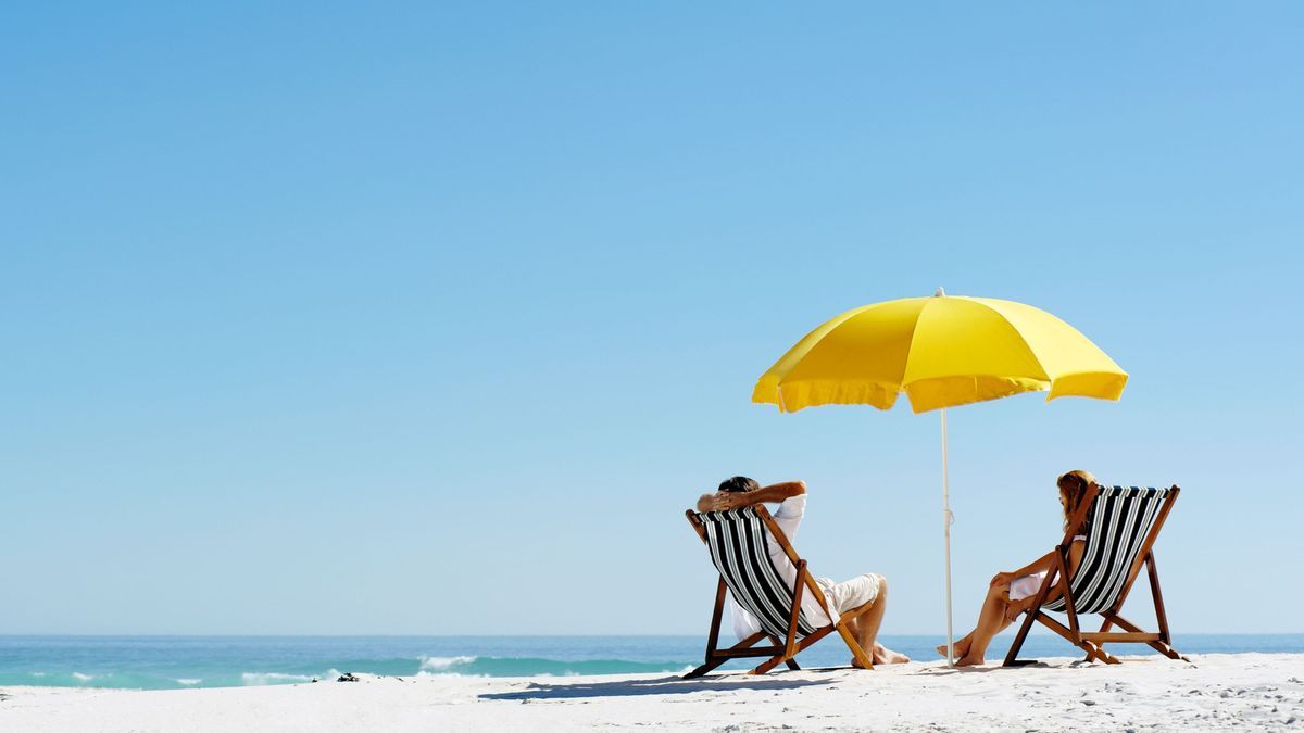 Strandsommerpaare entspannen sich in der Sonne auf ihren Klappstühlen unter einem gelben Regenschirm.