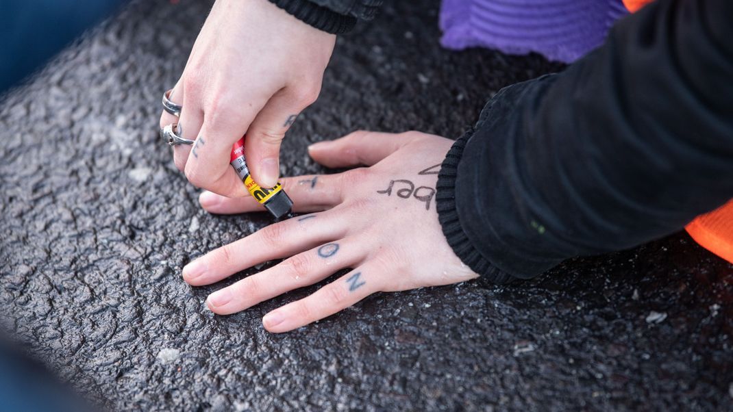 Aktivisten der "Letzten Generationen": Eine Aktivistin klebt ihre Hand mit Sekundenkleber am Asphalt fest.