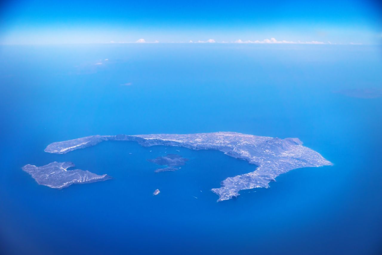 Santorin: Die Vogelperspektive zeigt die Ringstruktur der griechischen Insel. Diese ist der Überrest eines riesigen Vulkans, der hier rund 1.600 Jahre vor Christus explodierte. Auch gibt es durch den Vulkan die von Platon beschriebenen heißen Quellen und das fruchtbare Ackerland. 