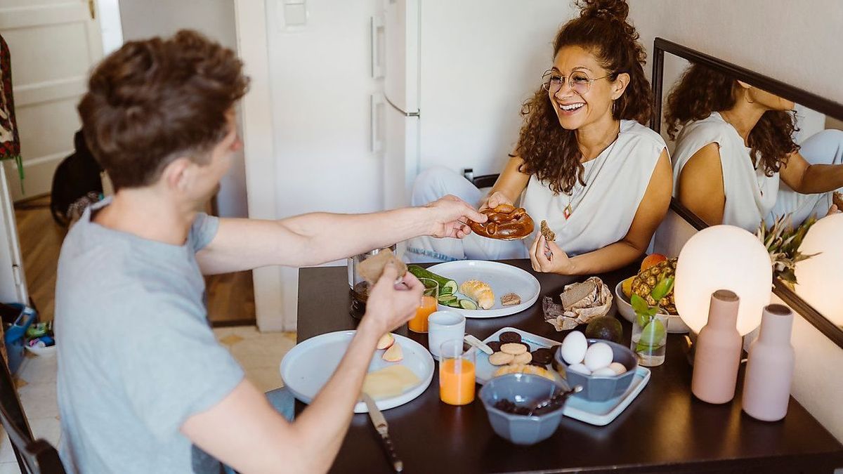 MASF34976 - Happy couple sharing food with each other while sitting on dining table at home