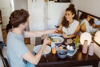 MASF34976 - Happy couple sharing food with each other while sitting on dining table at home