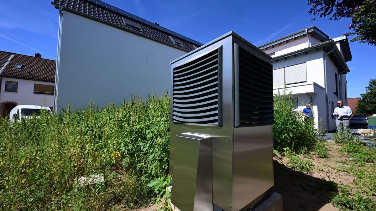 Vor einem neu gebauten Wohngebäude ist im Garten eine Wärmepumpe zum Heizen des Gebäudes in Betrieb. 