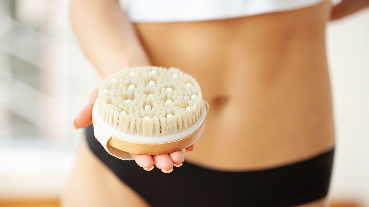 Woman arm holding dry brush to top of stomach leg