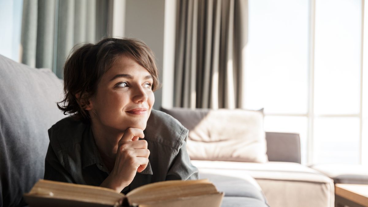 Image of caucasian cute pleased woman reading book and smiling