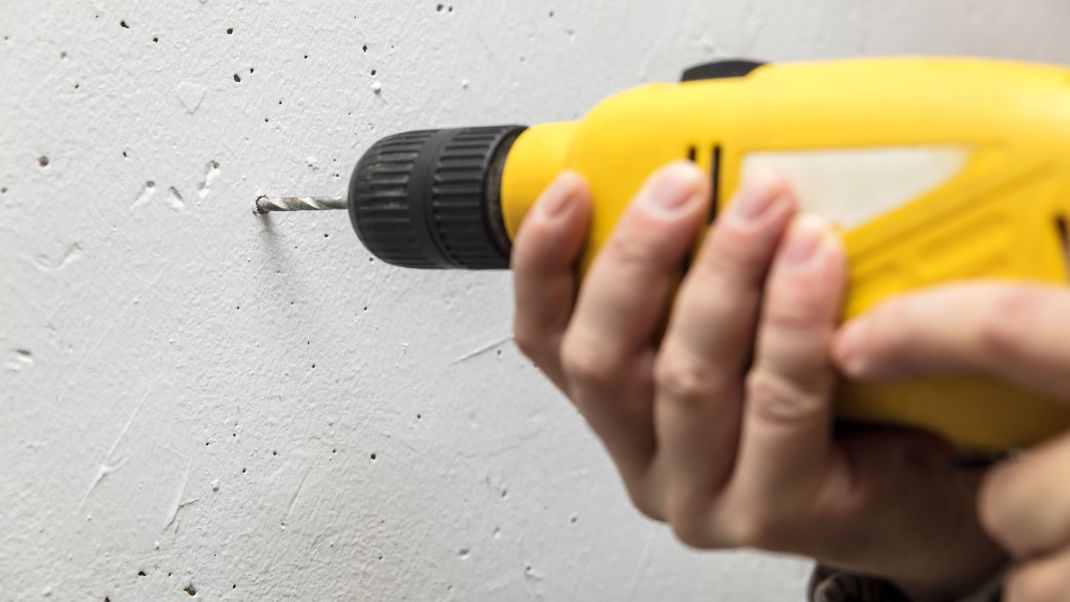 Heimwerker bohrt mit einer handlichen Bohrmaschine ein Loch in eine Wand aus Beton.