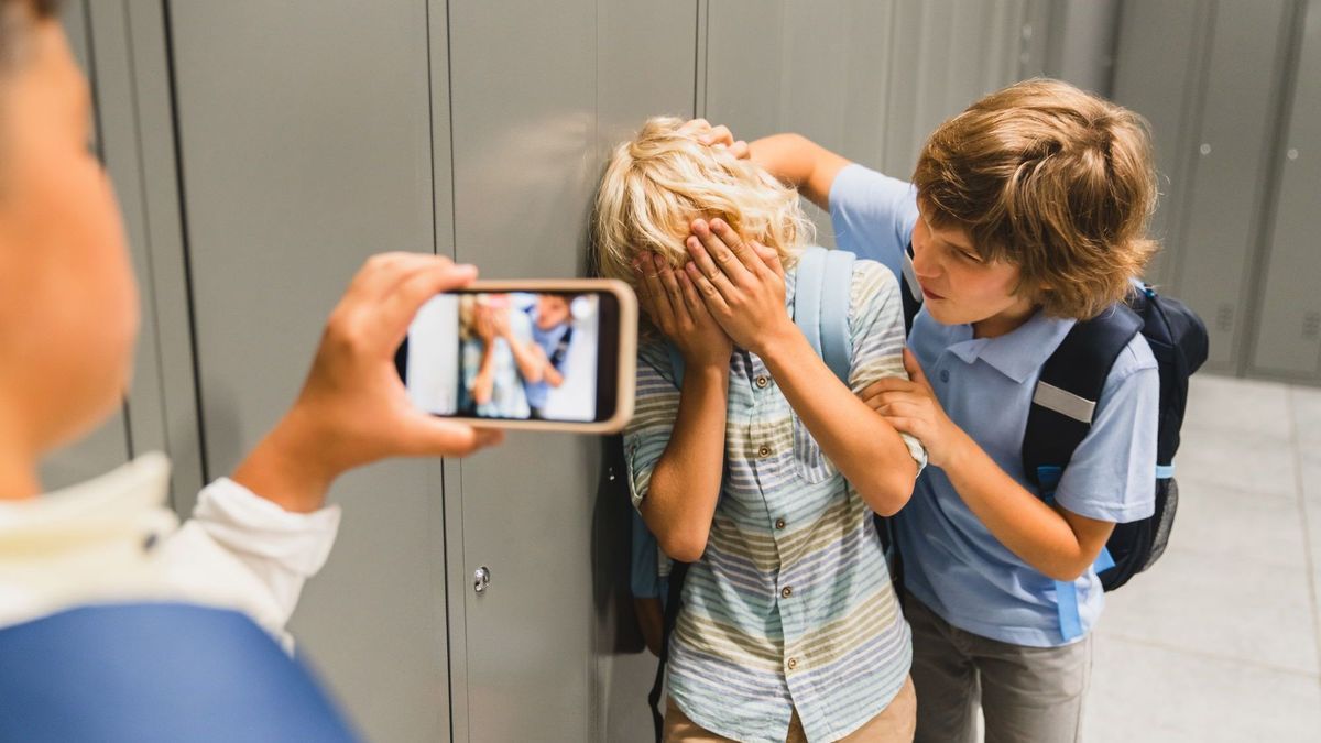 Schulkinder, die grausame Jungen am Telefon filmen, wie sie ihren Klassenkameraden in der Schulhalle foltern. Pubertät schwieriges Alter