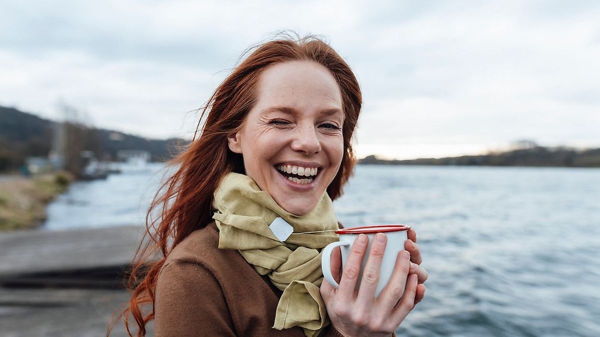 Happy woman with tea cup by lake on weekend Frau mit Tee