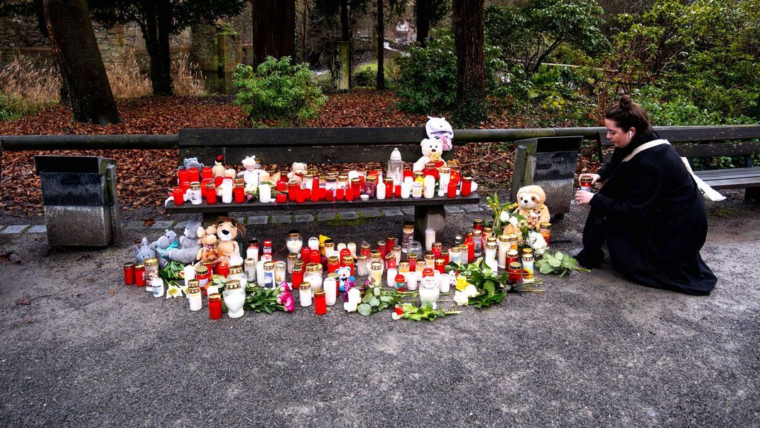 Eine Frau stellt eine Trauerkerze neben Blumen und Kuscheltieren im Park Schöntal auf, nachdem am 22. Januar 2025 in Aschaffenburg zwei Menschen, darunter ein Kind, bei einem Messerangriff getötet wurden,