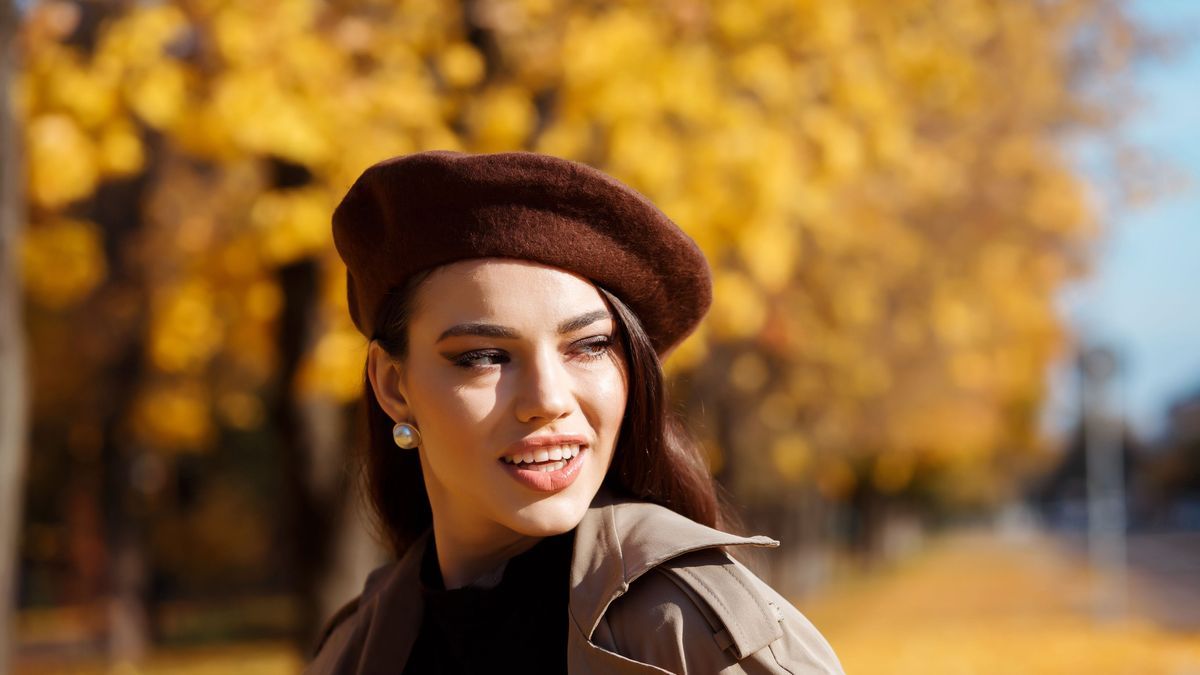 Stylish woman in brown beret outdoors in the park in fall season, yellow leaves bokehbackground.