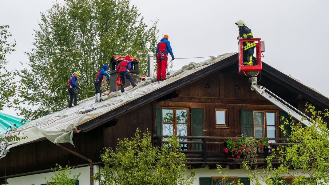 Feuerwehrleute sichern und decken beschädigte Dächer mit großen Planen ab. 