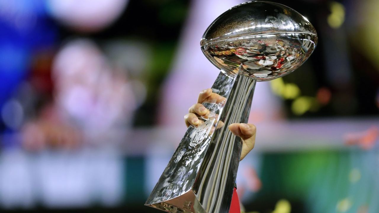 Die Trophäe: Die Vince Lombardi Trophy, benannt nach dem erfolgreichen Trainer der Green Bay Packers, Vincent Thomas Lombardi, wurde fünfmal von ihm gewonnen, darunter die ersten beiden Super Bowls 1967 und 1968. Anders als ein Wanderpokal behalten die Sieger die 55 Zentimeter große und 3,5 Kilo schwere Trophäe aus Sterling-Silber, hergestellt von Tiffany &amp; Co. Sie hat einen Wert von rund 25.000 Dollar.