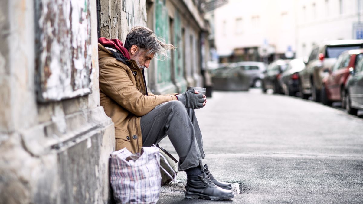 Homeless beggar man sitting outdoors in city asking for money donation.